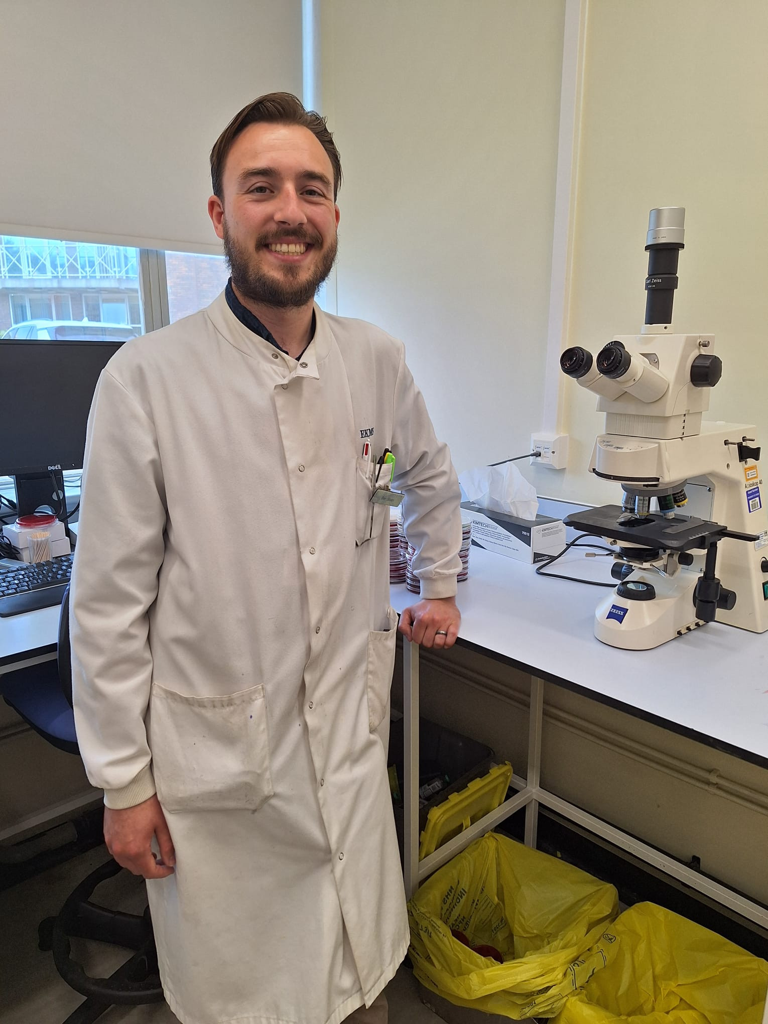 Ben Sloan standing in a lab coat by a microscope