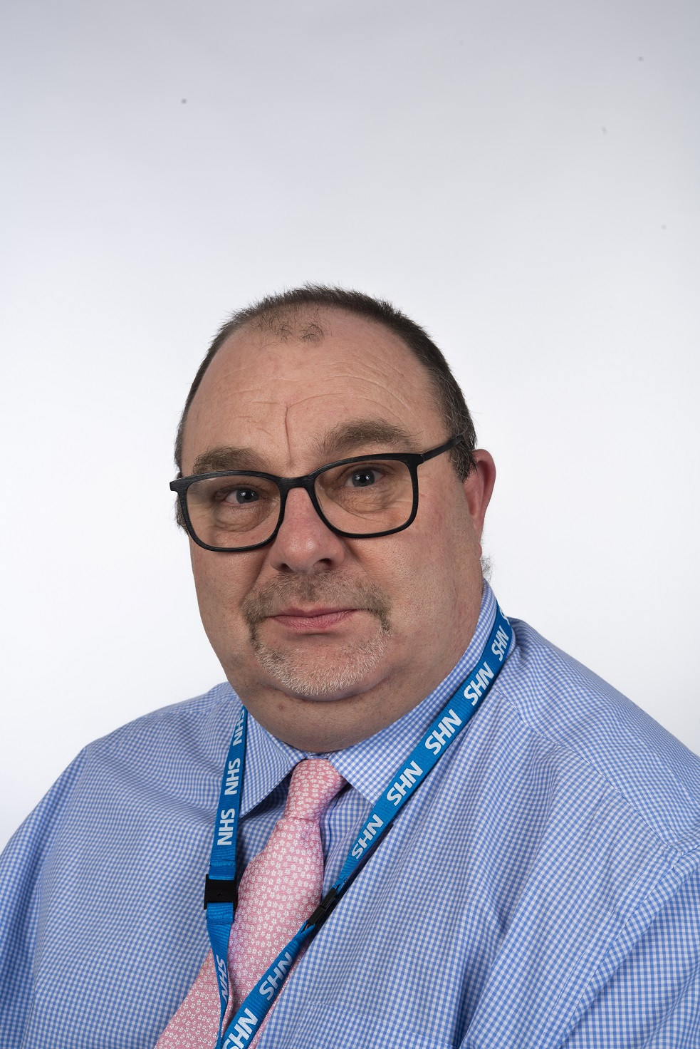 Carl Plummer, Trust Governor who has been appointed to a national role. Head and shoulders image, he is wearing a blue shirt pink tie and NHS lanyard