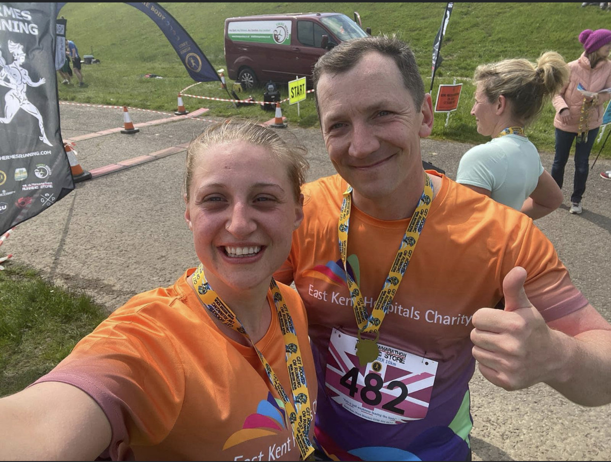 Megan Little and Chris Rowsell. They are wearing orange East Kent Hospitals Charity t-shirts with medals round their necks and are smiling at the camera in a selfie pose.