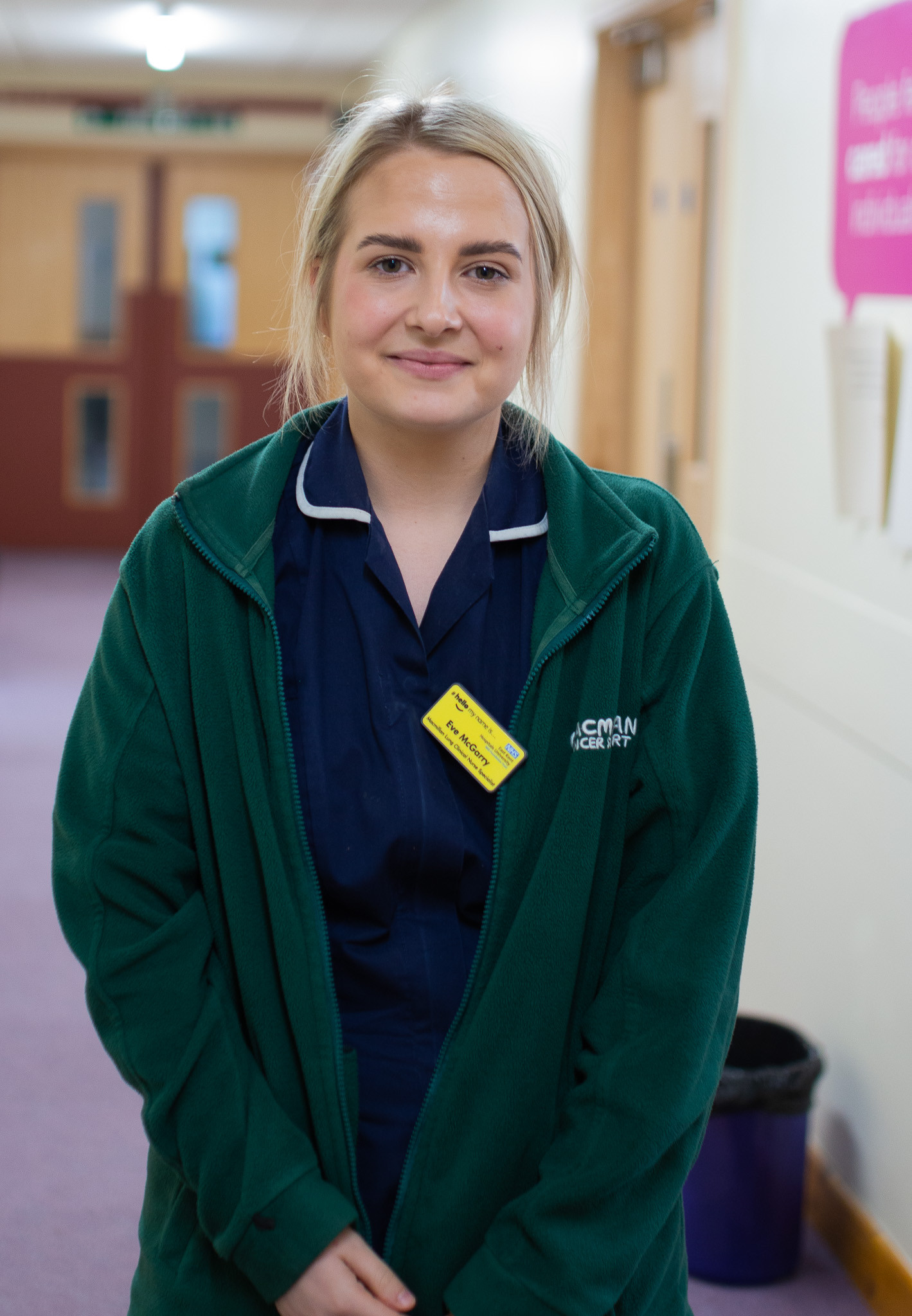 Eve McGarry, lung cancer CNS nurse. She is pictured in a corridor wearing a uniform and fleece and yellow name badge
