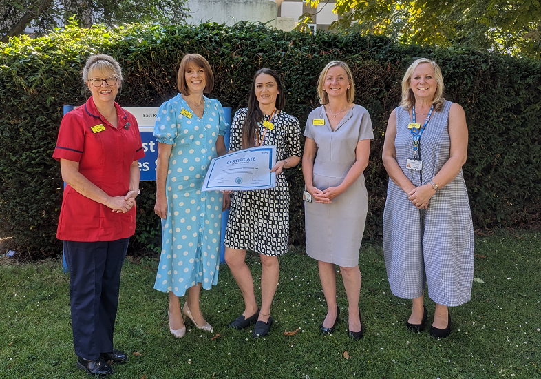 Holly Starling-Cass, centre, with Andrea Ashman, to her left, and Julie Yanni, left, and two other team members with the award. They are standing in a garden area with a hedge behind them. Julie is wearing a uniform, the others are not.