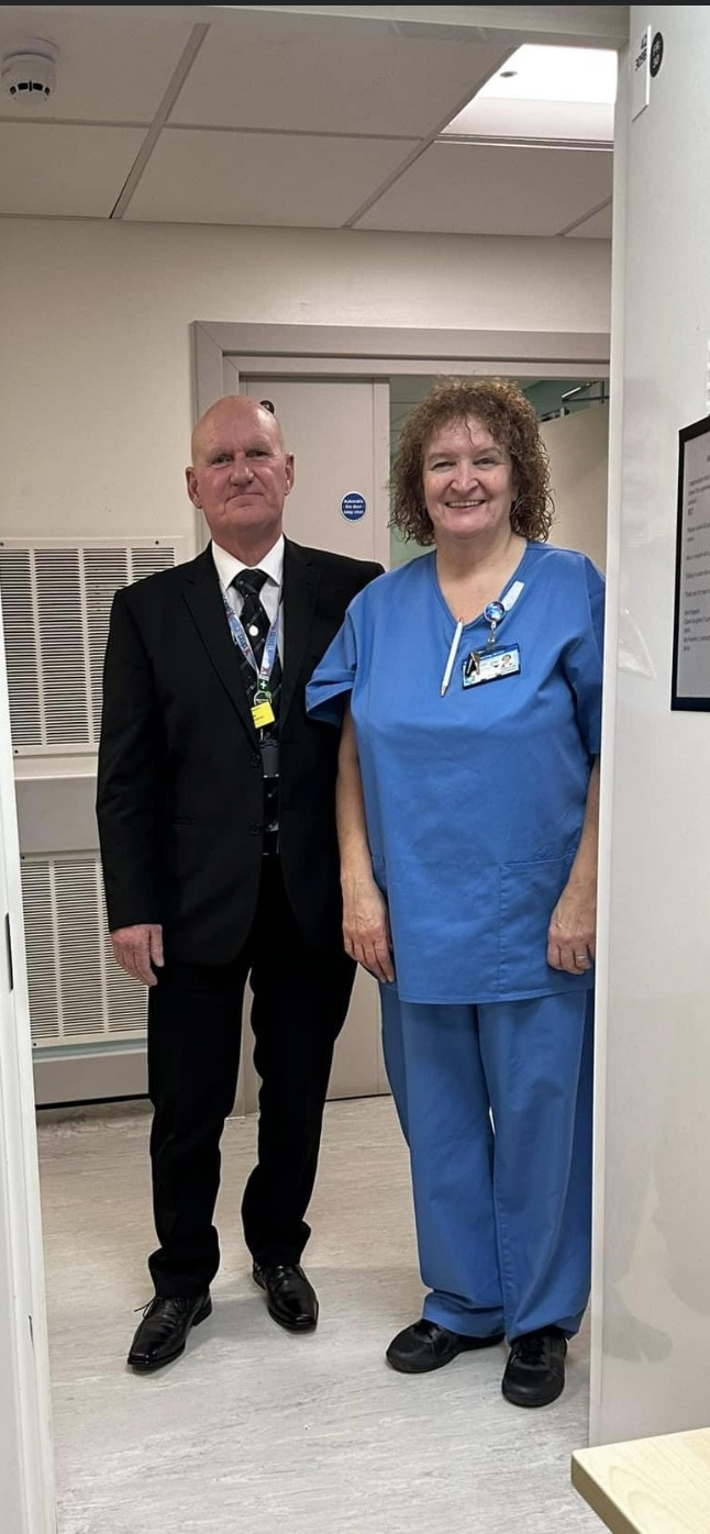 Husband and wife Ian and Mo Peebles. She is wearing scrubs, he is wearing a suit