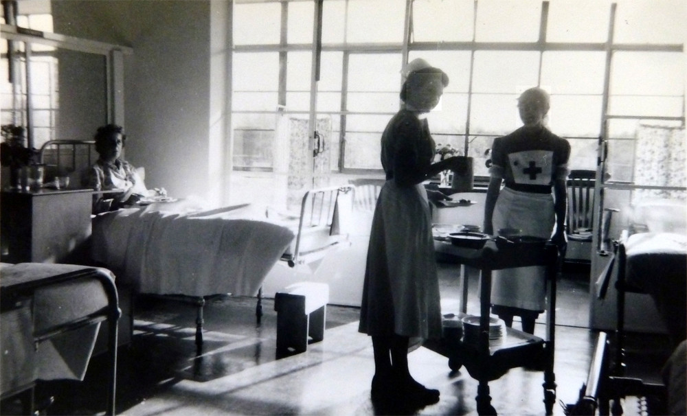 Mount McMaster ward in 1963 - image shows an old-fashioned ward with a patient in bed and two nurses with a tea trolley