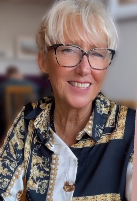 Rosemary Bevans. She is wearing a patterned blouse and glasses and smiling at the camera