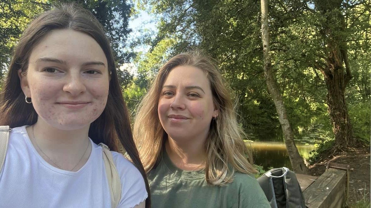 Ruth and Danielle during one of their walks. Selfie image in woodland with a river behind them.