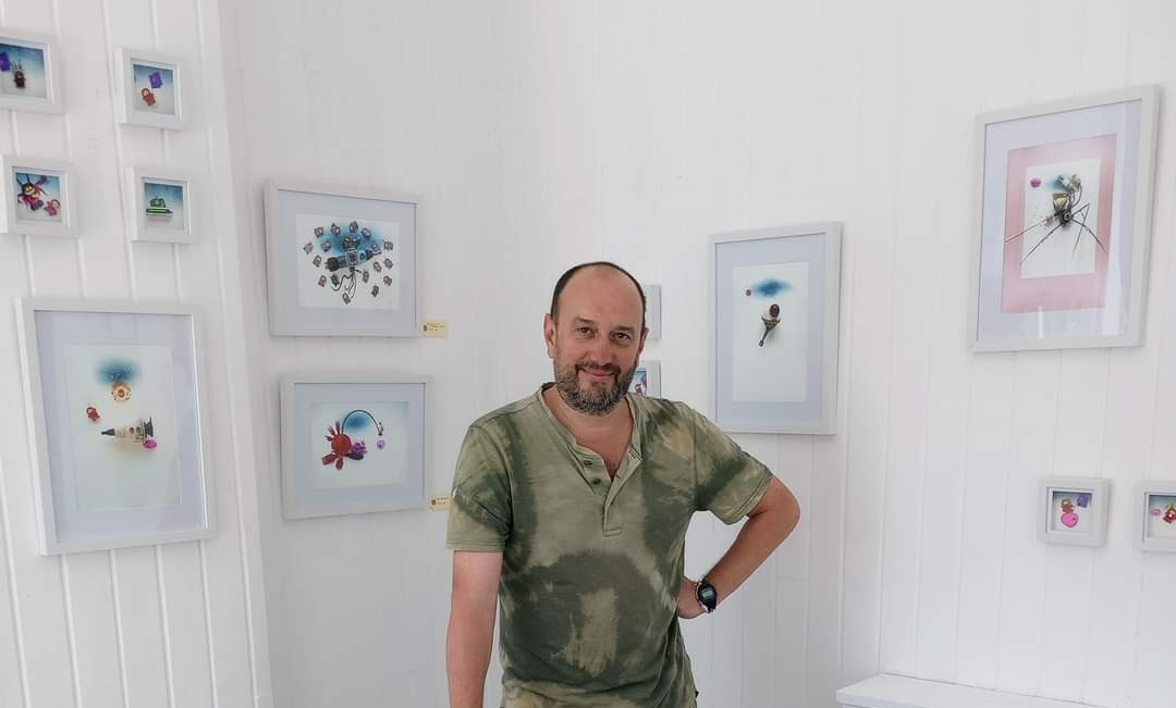 Ryan Harris, who is staging an exhibition showcasing his tiny space creatures. He is pictured in a room with images featuring the models displayed on the walls.