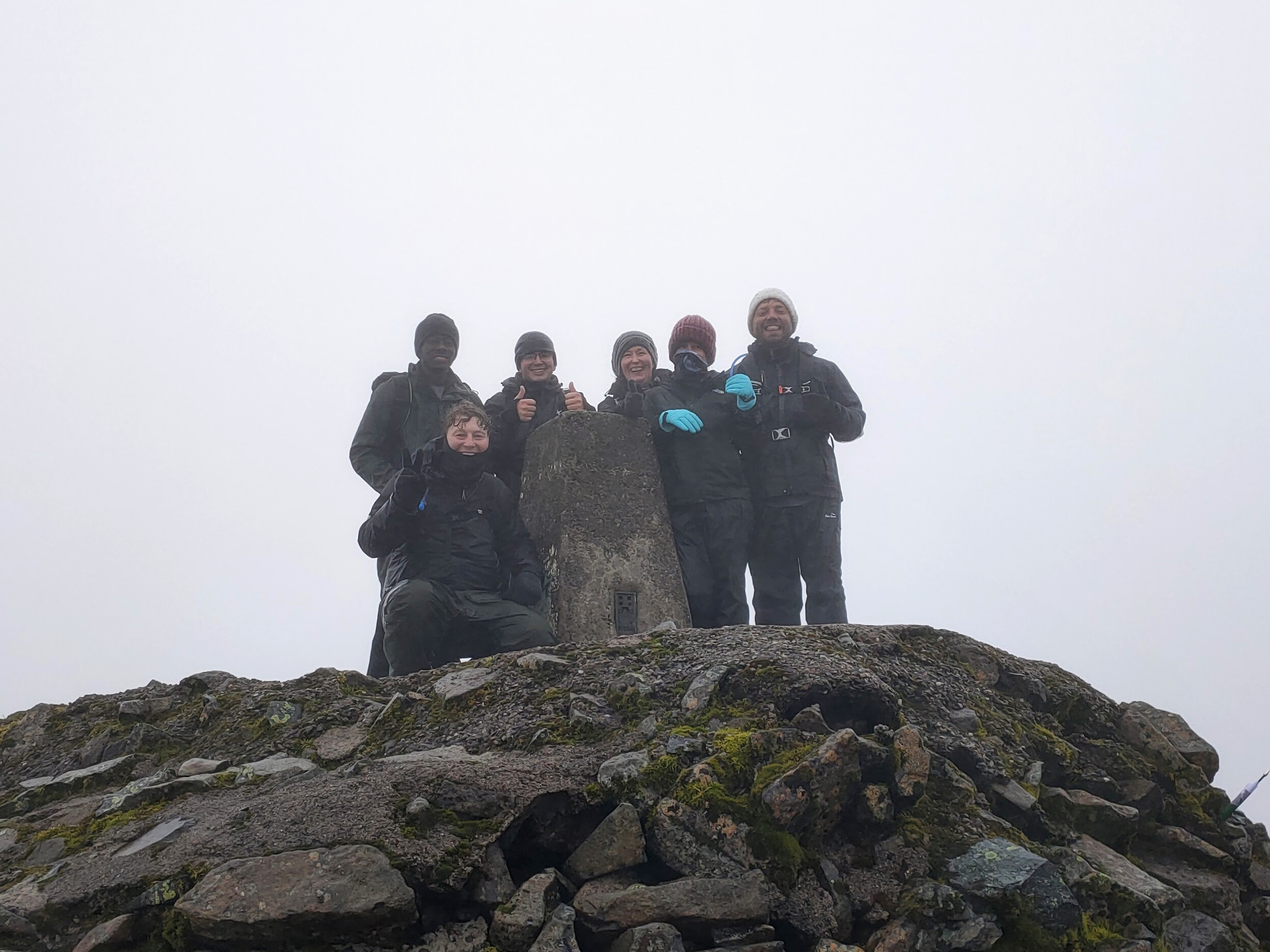 The team at the top of Ben Nevis. Image is six people on top of a craggy summit, wearing wet weather gear