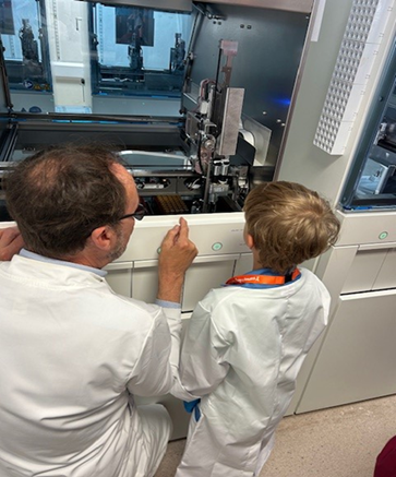 Thomas is shown some of the equipment in the lab by a male worker - both wearing lab coats